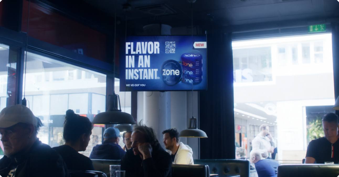 Guests at a shopping-centre restaurant under a screen playing a drinks advertisement